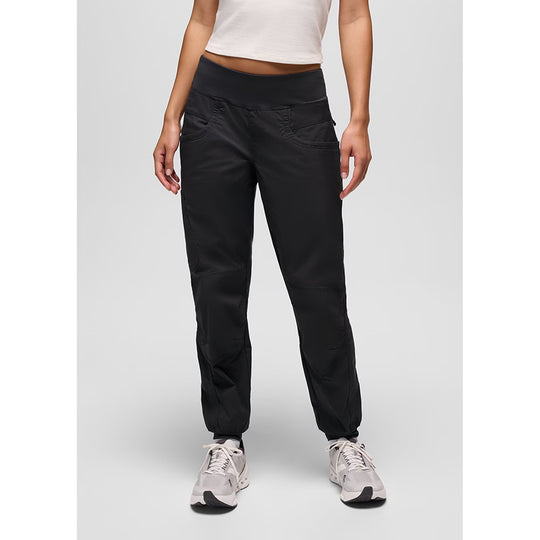 A model from the waist down wearing black athletic jogger pants with zippered pockets and elastic cuffs, paired with light gray sneakers on a light gray studio background.