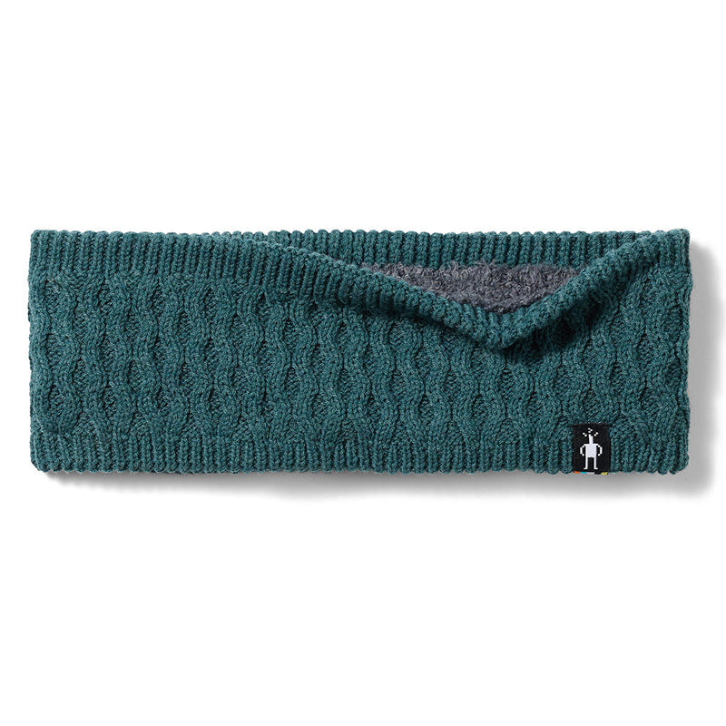 A dark teal cable-knit headband with a folded-over flap showing a gray inner lining, photographed flat on a white background. A small black brand tag is visible on the bottom right.