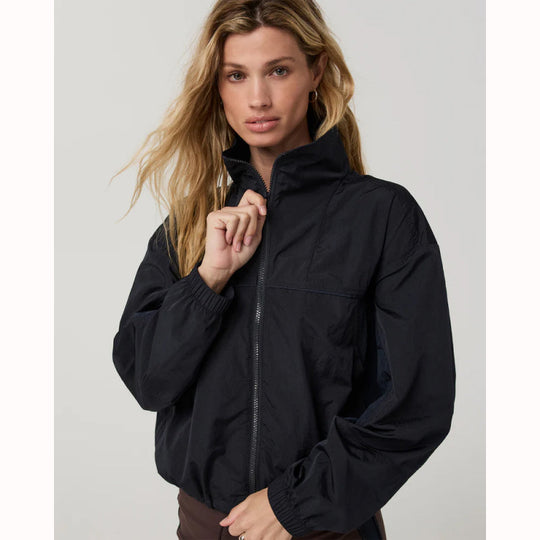 A woman wearing a black lightweight zip-front jacket with elasticized cuffs and a stand collar, posed against a light gray studio background.