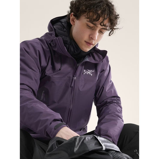 Person wearing a purple jacket with a brand logo, sitting on a light-colored background