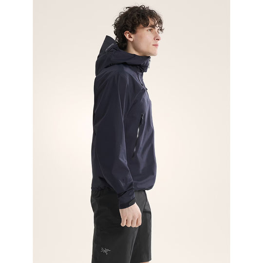 Person wearing a dark blue jacket with a hood on a light beige background