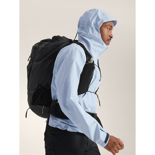 Person wearing a light blue hooded jacket with a black backpack on a beige background