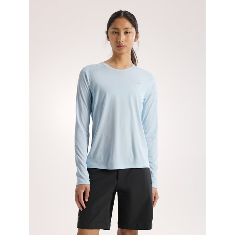Person wearing a light blue long-sleeve shirt and black shorts on a white background