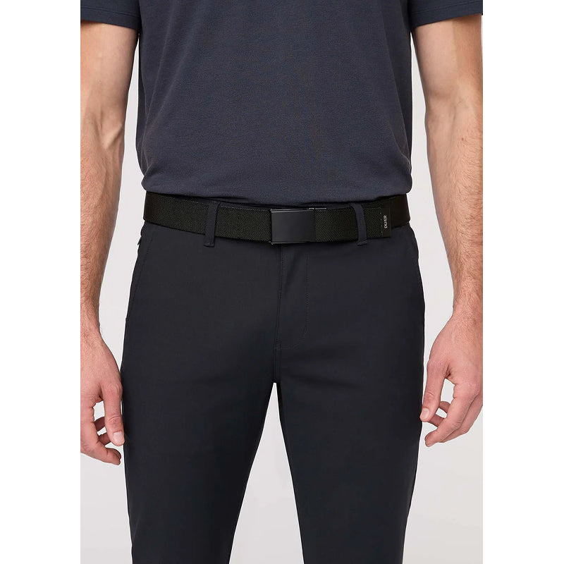 A man wearing slim-fit black dress pants, a black belt, and a dark navy short-sleeve polo shirt, shown from the chest down against a light gray studio background.