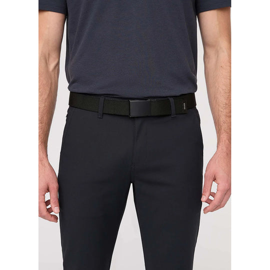 A man wearing slim-fit black dress pants, a black belt, and a dark navy short-sleeve polo shirt, shown from the chest down against a light gray studio background.