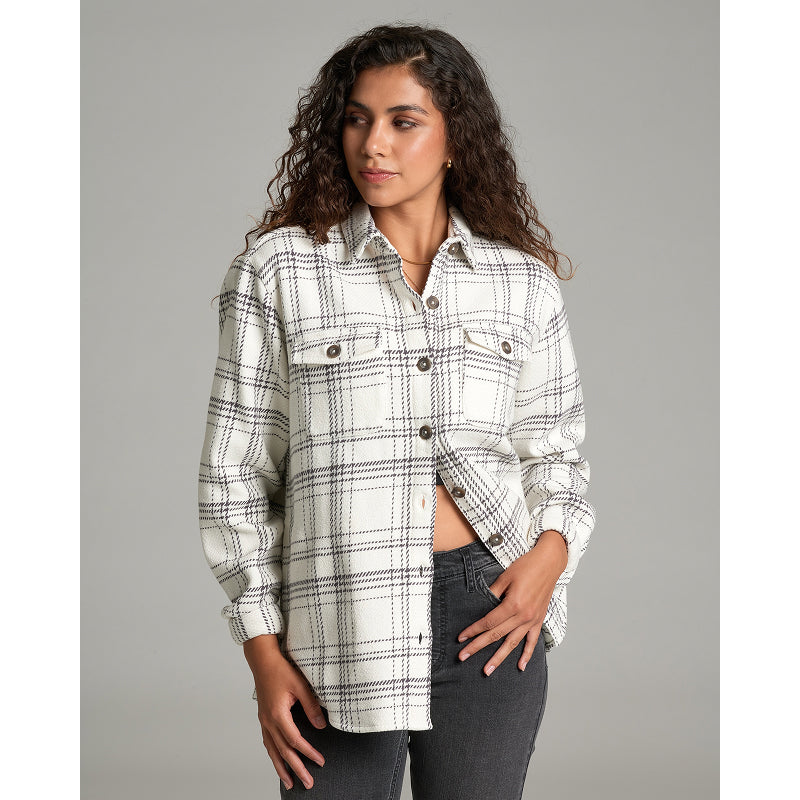 A woman modeling a long-sleeve plaid button-up shirt in off-white with black and gray lines, paired with dark gray jeans, against a solid gray studio background.