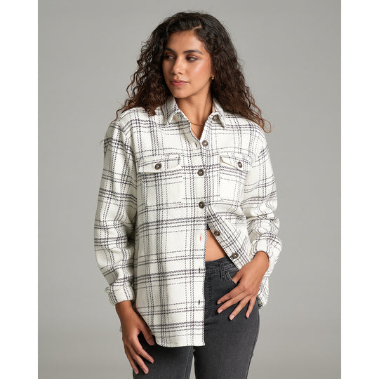 A woman modeling a long-sleeve plaid button-up shirt in off-white with black and gray lines, paired with dark gray jeans, against a solid gray studio background.