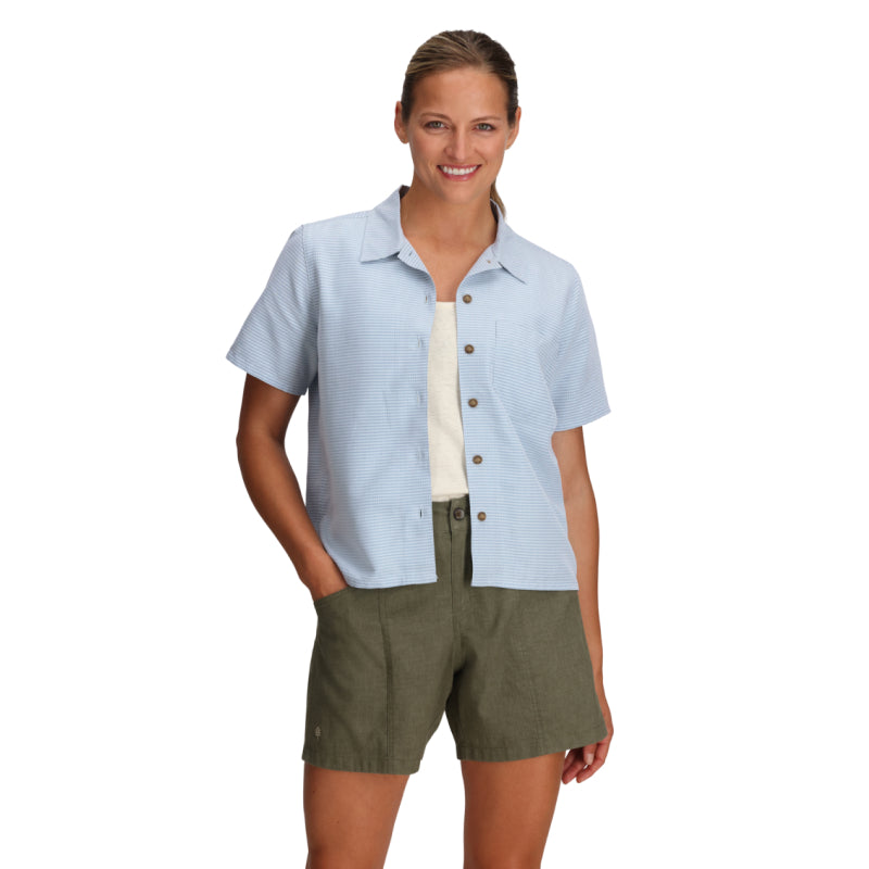 Woman wearing a light blue shirt with short sleeves and green shorts on a white background