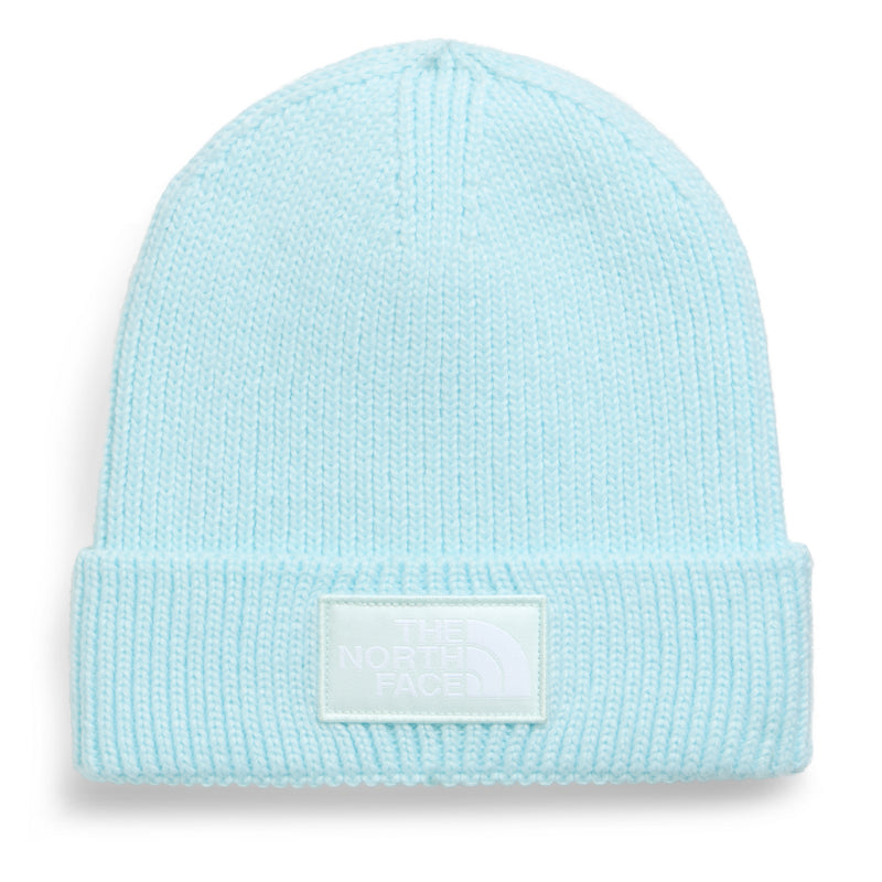 A light pastel blue knit beanie hat with a folded cuff and a white rectangular patch on the front that reads &