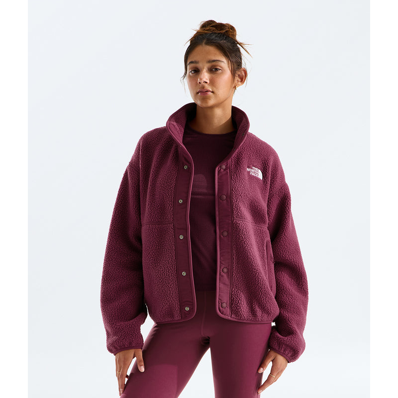 A woman modeling a maroon fleece button-front jacket with a small white embroidered The North Face logo on the chest, paired with matching maroon leggings and a top, against a light gray studio background.