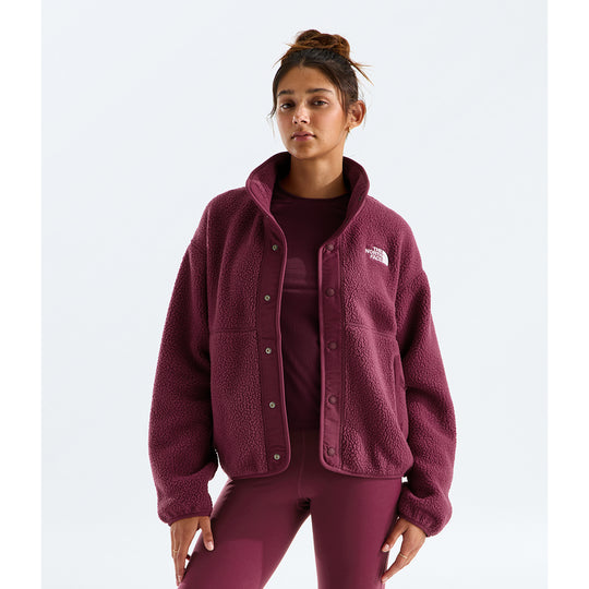 A woman modeling a maroon fleece button-front jacket with a small white embroidered The North Face logo on the chest, paired with matching maroon leggings and a top, against a light gray studio background.