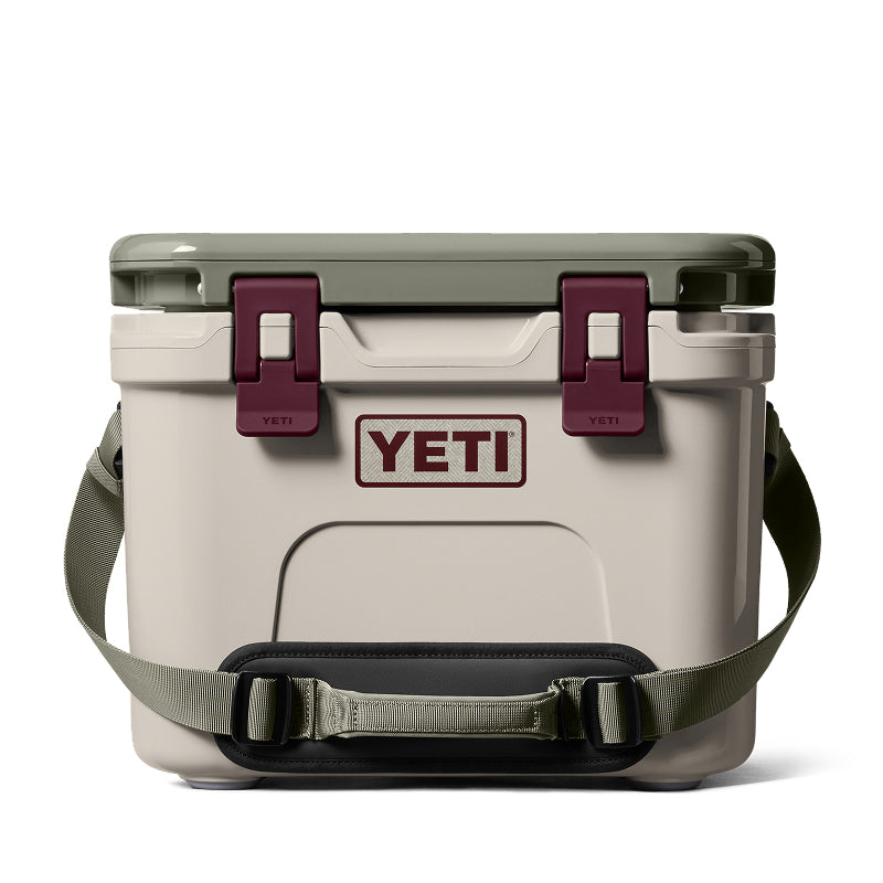 A YETI cooler with a light beige body, olive green lid and shoulder strap, and dark burgundy latches and handle pad, shown on a clean white background.