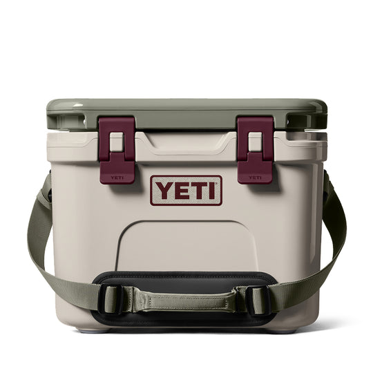 A YETI cooler with a light beige body, olive green lid and shoulder strap, and dark burgundy latches and handle pad, shown on a clean white background.